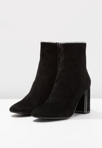 Black suede ankle boots with a pointed toe and a silver-accented block heel. Features a side zipper for closure. Smooth texture.