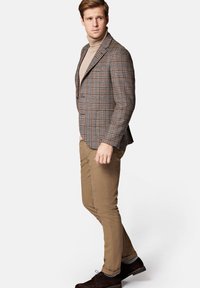 Brązowa marynarka w kratę z zapięciem na dwa guziki, połączona z beżowym golfem, brązowymi spodniami i ciemnym obuwiem. Slim fit z dopasowanym krojem.