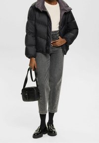 Giacca nera voluminoso con colletto grigio, abbinata a jeans grigi a vita alta, mocassini neri e una piccola borsa a tracolla nera.