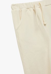 Krämfärgade sweatpants med mjuk textur, elastisk midja, snörningsdetalj och sidofickor. Enkelt design utan mönster.