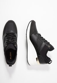 Baskets noires ALDO avec design à lacets, semelles épaisses blanches et accent doré au talon, vues de dessus et de côté sur fond blanc.