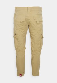 Beige cargo pants made of cotton, featuring side pockets, a relaxed fit, visible stitching, and a red tag at the hem.