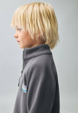 Pullover in pile grigio con colletto alto, dotato di zip e toppa con logo sul petto. Texture morbida, design minimalista.