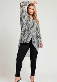 Lekka, przezroczysta bluzka w czarno-białe wzory z długimi rękawami, dekoltem w kształcie litery V oraz asymetrycznym dołem, w połączeniu z czarnymi wąskimi spodniami i szpilkami.