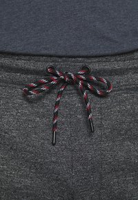 Grijze joggers van een gestructureerde stof, met een zwarte trekkoord voorzien van rood, wit en blauwe strepen, vastgezet met zwarte plastic punten.