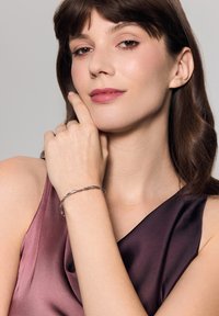 Srebrna bransoletka o skręconym wzorze, z małymi błyszczącymi akcentami. Noszona na ręce, w połączeniu z sukienką o satynowym wykończeniu w ciemnych odcieniach.