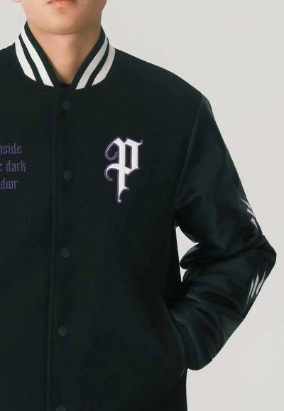 Giacca varsity nera con colletto a righe bianche, lettera "P" ricamata di colore viola e dettagli stilizzati sulle maniche. Texture liscia.