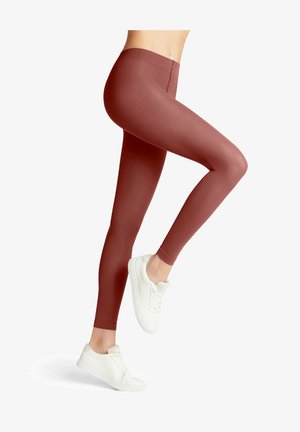 Bordeauxfarbene Leggings aus elastischem Material, mit einem hohen Bund und einem glatten, enganliegenden Design. Kombiniert mit weißen Sneakers.