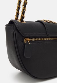 Musta nahkainen olkalaukku, jossa on kaareva muoto, kultasävyinen ketjuhihna, vetoketjusuljin ja koristeelliset niitit läpällä. Rakenne on teksturoitu.