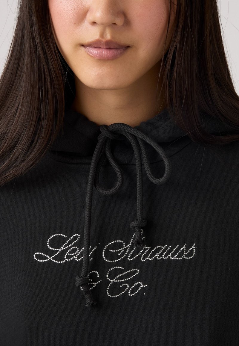 Hoodie noir avec cordon de serrage ajustable, mettant en avant un texte en strass argentés "Levi Strauss & Co." à l'avant. Texture douce et design décontracté.