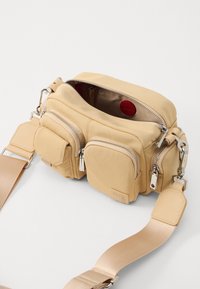 Borsa a tracolla beige realizzata in nylon morbido, con due tasche anteriori con zip, un compartimento principale con zip e una tracolla in tessuto piatta.