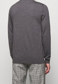 Pull en laine gris à manches longues, col rond et poignets côtelés, associé à un pantalon à carreaux dans des nuances de gris et crème.