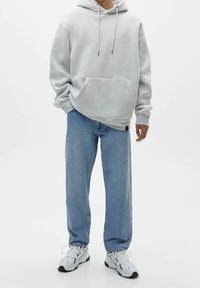 Světle šedá mikina s kapucí, přední kapsou, stahovacími šňůrkami a žebrovanými manžetami, doplněná světle modrými džíny s přímými nohavicemi a bílými teniskami.