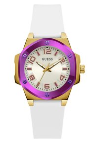 Lila und goldene achteckige Uhr mit weißem Silikonarmband. Sie verfügt über ein cremefarbenes Zifferblatt, lila Stundenmarkierungen und goldfarbene Zeiger. Modell: Guess.