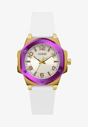 Montre octogonale violette et dorée avec un bracelet en silicone blanc. Elle possède un cadran crème, des index d'heure violets et des aiguilles dorées. Modèle : Guess.
