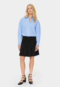 Camicia azzurra chiaro con un motivo testurizzato, abbinata a una gonna plissettata nera e scarpe con tacco a blocco nere.