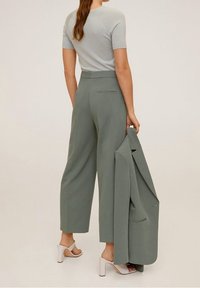 Pull court à manches courtes vert clair associé à un pantalon large dans une teinte assortie. Le mannequin tient une veste tailleur, mettant en avant un design minimaliste.