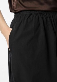 Melnas bikses ar elastīgu jostasvietu un sānu kabatu. Izgatavotas no viegla auduma, ar gludu virsmu un brīvu piegriezumu.