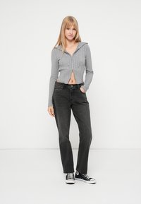 Šedá zkrácená mikina na zip s žebrovaným vzorem, doplněná o černé džíny s vysokým pasem a volným střihem a černé tenisky Converse.