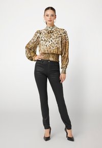 Blusa de estampado de leopardo con cuello alto y cintura fruncida, combinada con pantalones negros ajustados y tacones negros puntiagudos. Tejido suave y diseño estructurado.