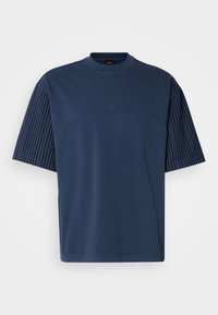 Camisa de manga corta azul marino con cuerpo liso y mangas de rayas texturizadas. Presenta un cuello redondo acanalado y un discreto detalle de logo.