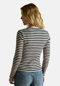 Dlhý rukáv pruhovaný top s námorníckymi a krémovými horizontálnymi pruhmi, rebrovanou textúrou a okrúhlym výstrihom, kombinovaný s modrými džínami.