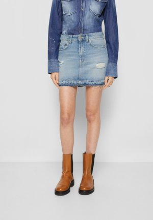 Saia de denim mini com lavagem azul clara, detalhes desgastados, bainha desfiada, combinada com botas de couro castanho até ao tornozelo e uma camisa de denim azul.