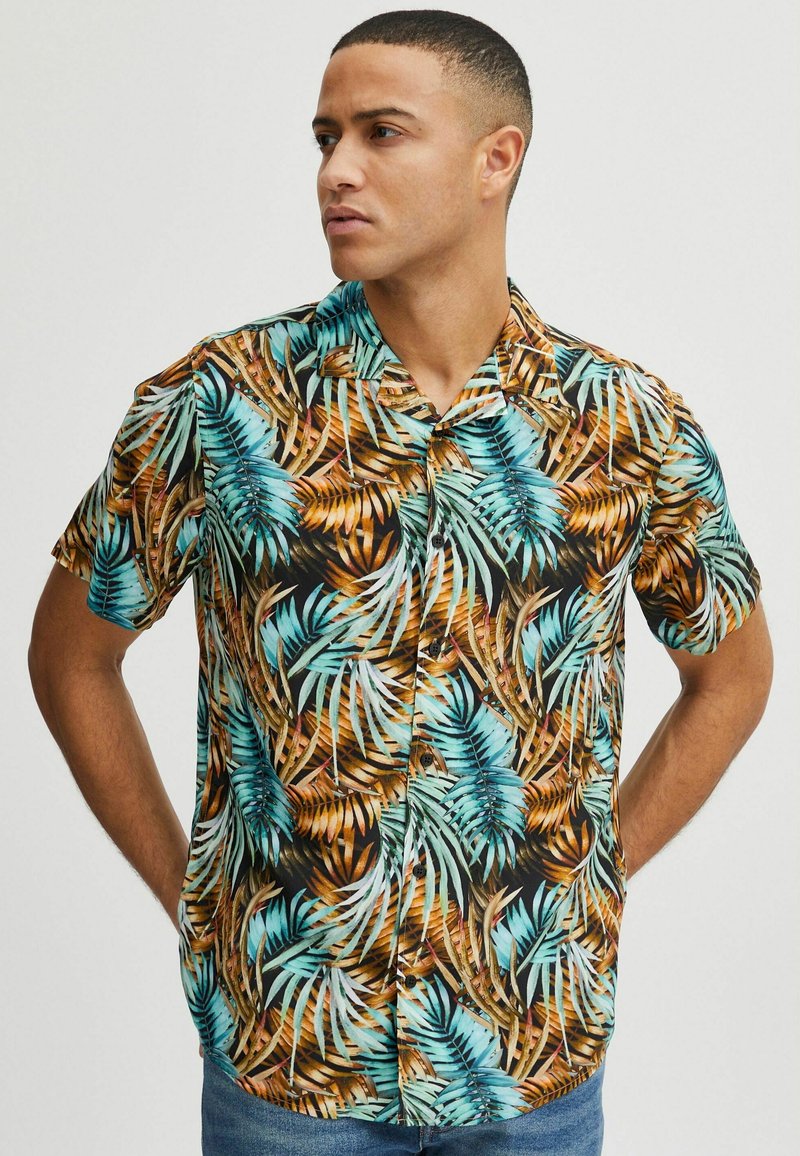 Chemise à manches courtes avec un motif de feuilles tropicales en bleu et marron sur fond noir, fabriquée en tissu léger et dotée d'un devant à boutons.