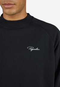 Sort sweatshirt med ribbet rund hals, tætsiddende ærmer og hvid "Pegador" broderi på venstre bryst. Blød tekstur, afslappet design.