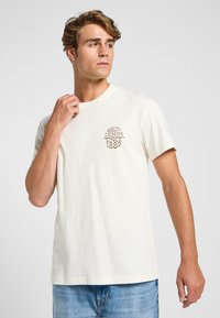Crème-kleurig T-shirt met korte mouwen, gemaakt van katoen, met een bruin geborduurd tekstontwerp met "QUALITY DENIM SINCE 1889."