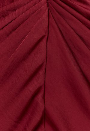 Tissu rouge profond avec des plis doux et des plis diagonaux convergeant vers le centre supérieur, mettant en valeur une texture lisse et un léger éclat.