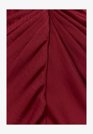 Giliai raudona audinys su minkštais klostėmis ir įstrižais raukšlėmis, susitelkiančiomis į viršutinį centrą, rodantis lygią tekstūrą ir subtilų blizgesį.