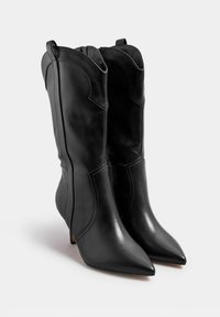 Musta nahkasaappaat nilkkamittaisilla, teräväkärkisillä kärjillä, lännen tyyliin inspiroituneella suunnittelulla, yksityiskohtaisella ompelulla ja kiiltävällä, hiotulla pinnalla.