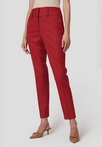 Czerwone dopasowane spodnie z wysokim stanem i wąskim krojem, wykonane z gładkiego materiału i z delikatnymi zagnieceniami. Połączone z beżowymi szpilkami w szpic.