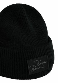 Svart stickad mössa med ribbat mönster och en mörk etikett i tyg med vit text. Rundad form med en tajt passform.