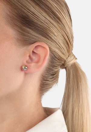 Primer plano de la oreja de una mujer con el cabello rubio recogido, que lleva un pequeño pendiente de botón bicolor en oro y plata.