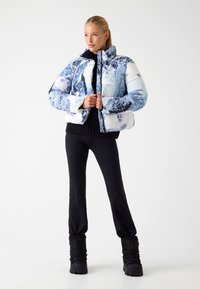 Puffy jack met een blauw-witte bergprint, hoge kraag en ritssluiting. Gemaakt in combinatie met zwarte aansluitende broek en gestructureerde laarzen.