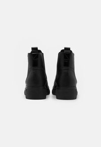 Black ankle boots made of textured leather with a thick rubber sole. Features a smooth pull tab and minimalistic design.