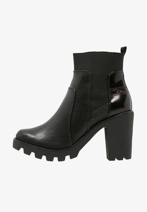 Botines negros con tacón grueso, que presentan cuero liso y texturizado, parte superior de tela elástica y costuras en un sutil acento rojo.