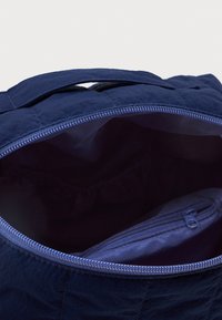 Ναυτικό μπλε τσάντα με χερούλι από πάνω και ανοιχτό φερμουάρ που αποκαλύπτει τον άδειο εσωτερικό χώρο και μία μικρή κλειστή τσέπη μέσα.