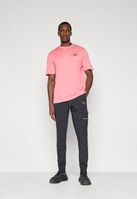 Ροζ αθλητική μπλούζα με υφή, συνδυασμένη με σκούρο γκρι παντελόνι καρό με πλαϊνές τσέπες και ελαστικά μανίκια. Μαύρα αθλητικά παπούτσια.