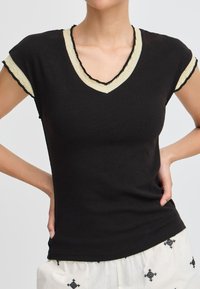 Tricou negru cu decolteu în V, cu mâneci scurte, având un tiv contrastant crem și negru pe marginea decolteului și a mânecilor. Material din bumbac.