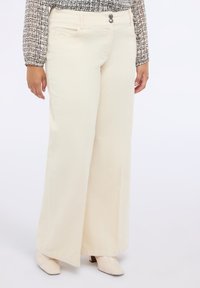 Pantaloni cream a gamba larga realizzati in tessuto morbido, dotati di due tasche anteriori, chiusura con zip e due bottoni, e cuciture minime.