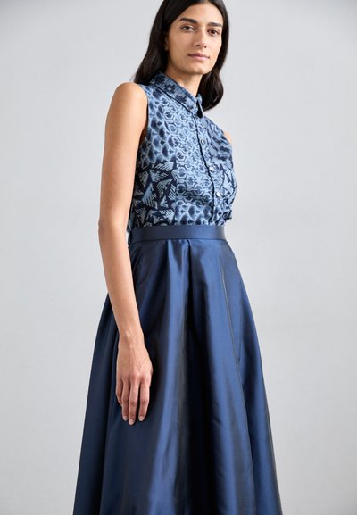 Vestido sin mangas con una parte superior texturizada azul que presenta patrones intrincados y una falda azul oscura y suave, ceñida en la cintura con una banda.