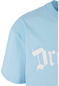 Lyseblå bomulds t-shirt med korte ærmer, prydet med fedt hvidt grafisk tekstdesign. Stoffet ser glat ud med en let glans.