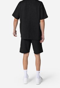 Maglietta nera a maniche corte con texture abbinata a pantaloni corti dello stesso colore. Indossata con sneakers bianche e calze, mostrando un fitting rilassato e un design semplice.