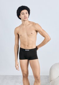 Fekete boxeralsó fehér "BOSS" logóval a derékrészen. A modell semleges háttér előtt áll, bemutatva a szabást és a dizájnt.