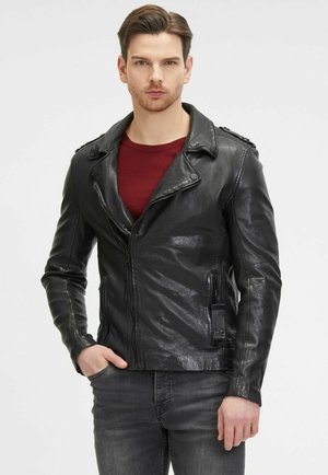Zwarte leren motorjack met ritssluiting, schouderepauletten en zijzakken. Draagt over een rode shirt, aansluitende stijl.