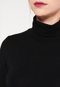 Svart rullekragegenser laget av elastisk stoff, med en tettsittende design og glatt tekstur, med en høy krage som rammer inn halsområdet.