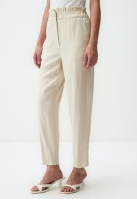 Pantalons beiges taille haute avec une coupe décontractée, devant plissé et poches latérales. Fabriqués en tissu léger avec une texture lisse.